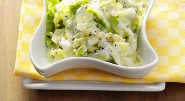 Cremiger Weißkohlsalat, ein einfaches wirsing rezept, serviert in einer weißen Schüssel auf gelb-weiß karierter Serviette.