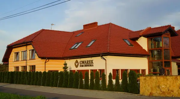 Dom Seniora Gwarek, nowoczesny budynek z czerwoną dachówką, otoczony zielenią.