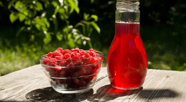 Maliny w misce i butelka soku malinowego. Zastanawiasz się, ile cukru do soku z malin?