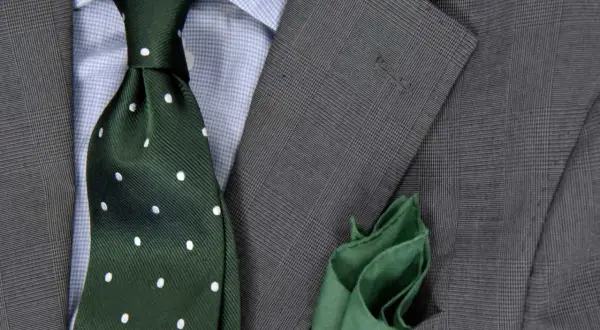 Zielony krawat w kropki do niebieskiej koszuli i szarej marynarki. Elegancka stylizacja.