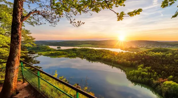 Vue panoramique depuis le belvédère Pic de l'Aigle au coucher du soleil, avec un lac reflétant le ciel et des collines verdoyantes.
