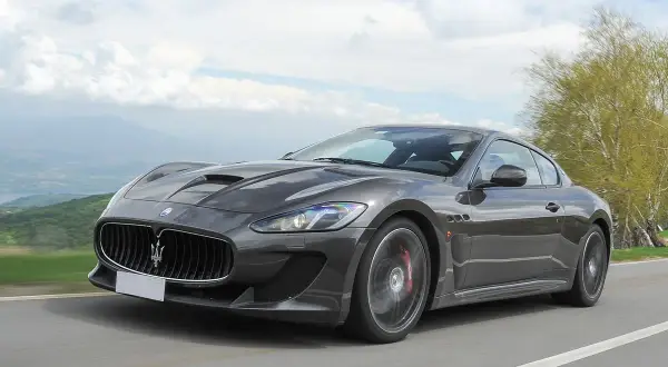 Szary Maserati GranTurismo na krętej drodze. Marzysz o takim aucie? Sprawdź aktualną maserati cena i spełnij marzenie.