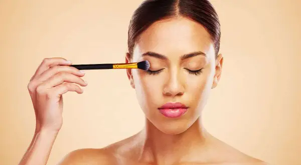 Donna applica ombretto con un pennello, un passo fondamentale per un make up perfetto.