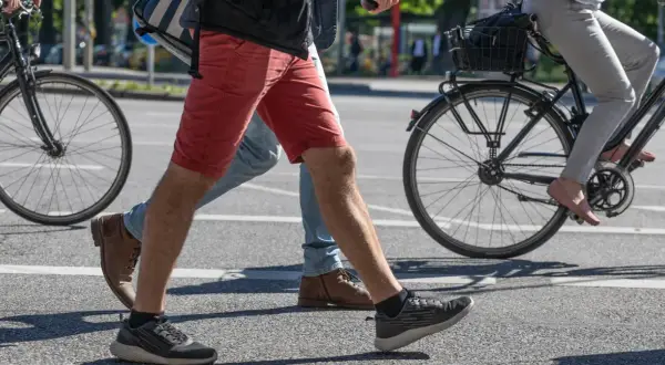 Ludzie przechodzą przez pasy, jeden na rowerze, drugi pieszo. Czy jazda na rowerze odchudza brzuch? To pytanie zadaje sobie wielu.