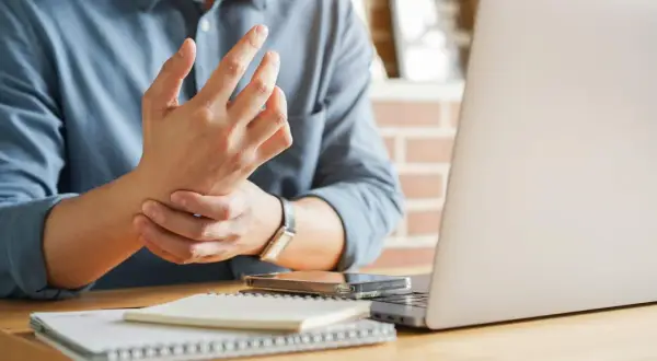 Uomo con male ai polsi mentre lavora al computer. Dolore al polso da uso prolungato del mouse e tastiera.