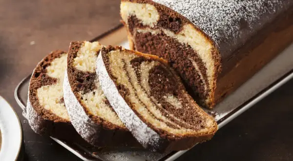 Pyszne ciasto zebra w keksówce, posypane cukrem pudrem, z kilkoma pokrojonymi kawałkami.