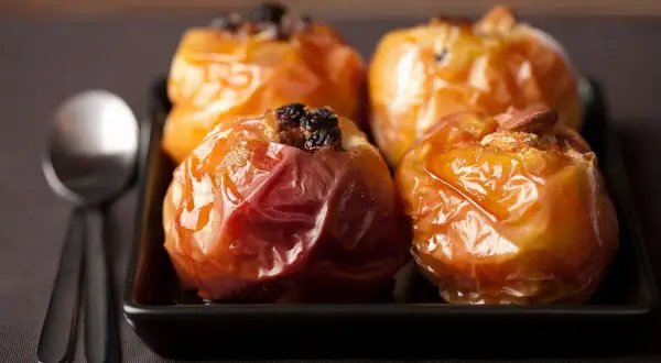 Mele cotte in friggitrice ad aria, caramellate e ripiene di uvetta e mandorle, pronte per essere gustate con un cucchiaio.