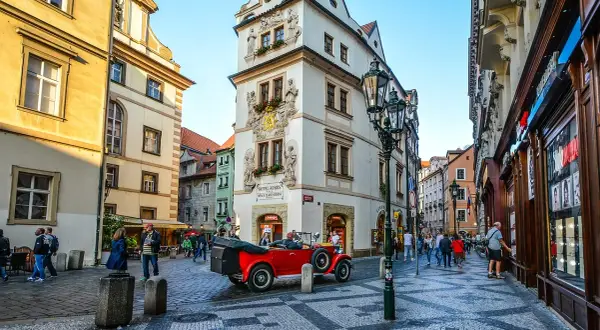Uliczka w Pradze z zabytkowym czerwonym kabrioletem i budynkiem z napisem "Hotel Aurus Dům Zlaté Střevy".