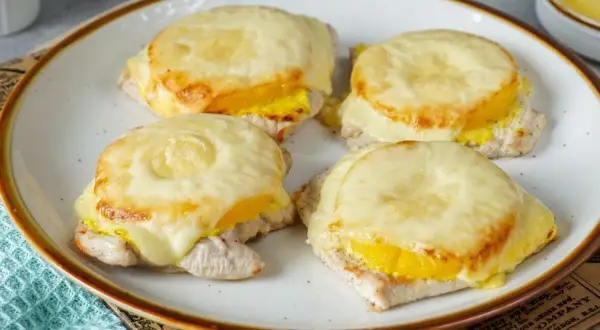 Vier saftige Schnitzel Hawaii mit geschmolzenem Käse und Ananasringen, appetitlich auf einem Teller angerichtet.