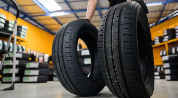 Deux pneus de voiture neufs, une sous-marque Michelin, sont présentés dans un entrepôt rempli de pneus.