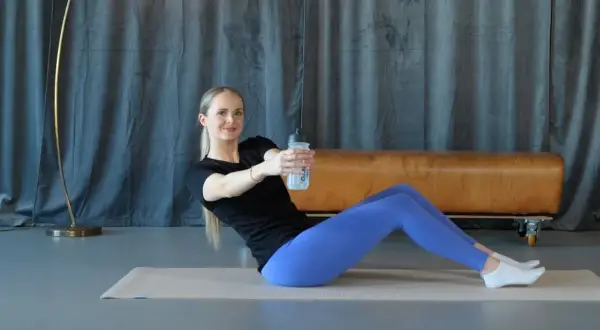 Frau macht isometrisches Training auf einer Matte, hält eine Wasserflasche und dreht den Oberkörper.
