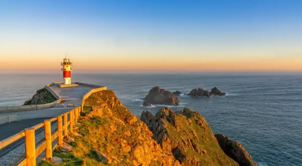 Faro en el cabo Ortegal al atardecer, con el mar azul y rocas emergiendo de las olas.