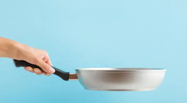 Dłoń trzyma aluminiową patelnię. Czy patelnia aluminiowa jest zdrowa? To pytanie nurtuje wielu kucharzy.