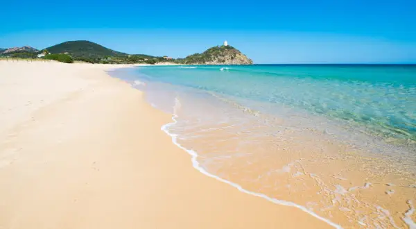 Piękne plaże Cagliari z turkusową wodą i piaszczystym brzegiem. W oddali widać wzgórze z wieżą.