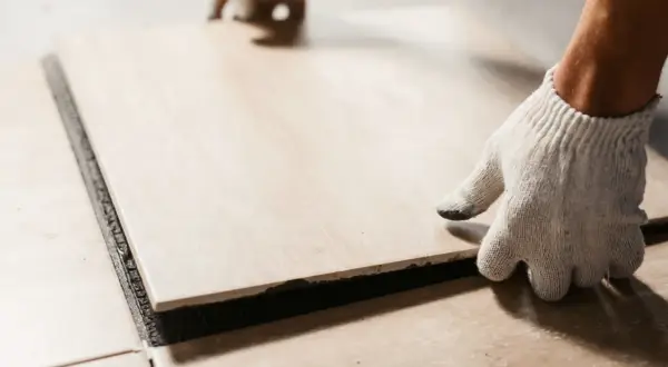 A gloved hand places a tile. Walking on tile too soon can cause shifting and unevenness.