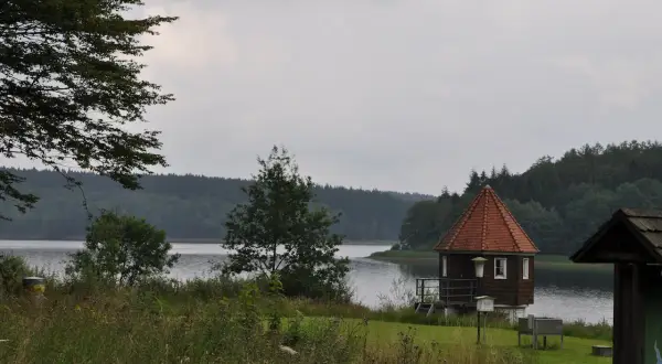 Kleines Holzhaus mit Spitzdach am Seeufer, ideal für einen Spaziergang auf dem kerspetalsperre rundweg.