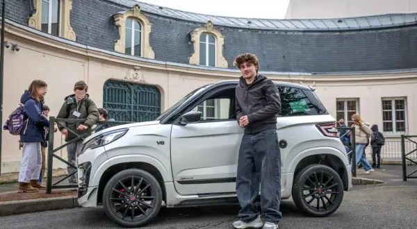 Un jeune homme pose à côté d'une voiturette électrique blanche. Le **rayon de braquage** de ce véhicule compact est idéal pour les rues étroites.