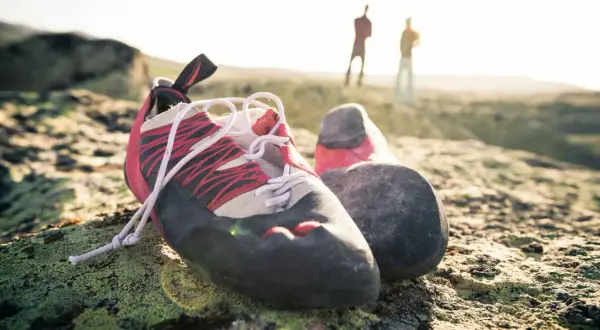 Kletterschuhe ruhen auf moosbewachsenem Fels. Im Hintergrund stehen zwei Kletterer. Zeit für kletterschuhe waschen.