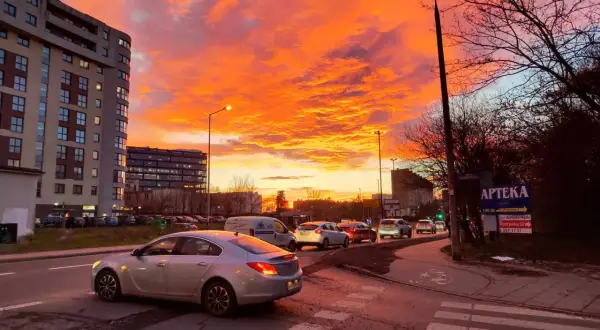 Spektakularny zachód słońca Kraków maluje niebo na pomarańczowo i różowo nad ulicą z samochodami i blokami.