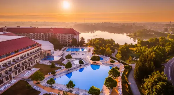 Widok z lotu ptaka na hotel z basenami i jeziorem o wschodzie słońca.