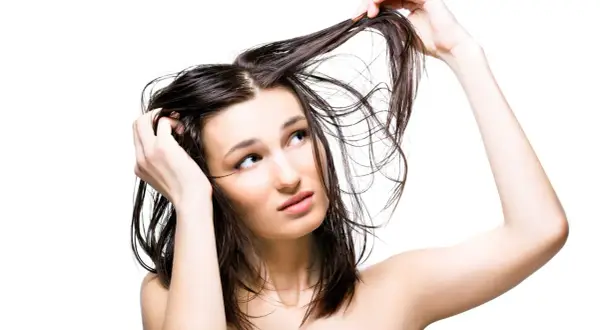 Jeune femme aux cheveux gras, se touchant la tête, l'air interrogateur. Pourquoi ces cheveux gras ?