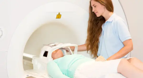 Pacjentka leży w aparacie do rezonansu magnetycznego, przygotowując się do tomografii głowy. Technik medyczny czuwa nad przebiegiem badania.