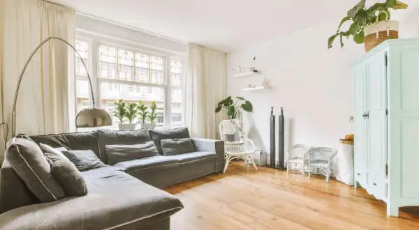 Gemütliches kleines Wohnzimmer einrichten mit großem Ecksofa, Bogenlampe, Pflanzen und mintgrünem Schrank.