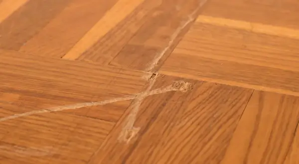 Gros plan sur un parquet en bois avec une rayure profonde et des éclats, témoignant d'une usure du temps.