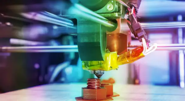 Głowica drukarki 3D drukuje brązową śrubę na platformie roboczej.