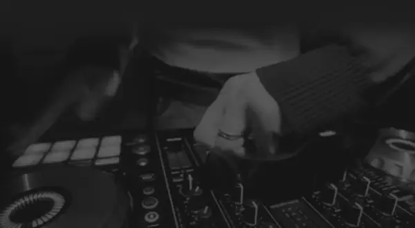 Dłoń DJ-a manipulująca pokrętłami na konsoli do miksowania muzyki.