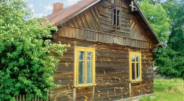 Stary drewniany dom z żółtymi oknami, otoczony zielenią. Zastanawiasz się, czym obić taki dom, by nadać mu nowy wygląd?