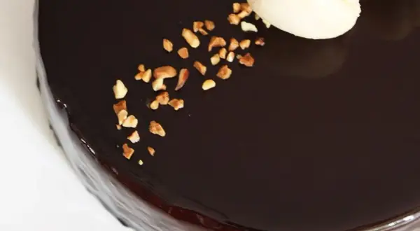 Gâteau au glacage chocolat brillant, parsemé de noisettes concassées et décoré de macarons.