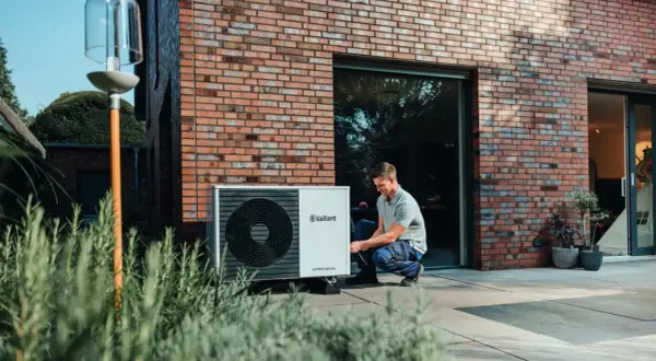 Installazione di una pompa di calore esterna: un uomo controlla l'unità posizionata vicino alla casa.