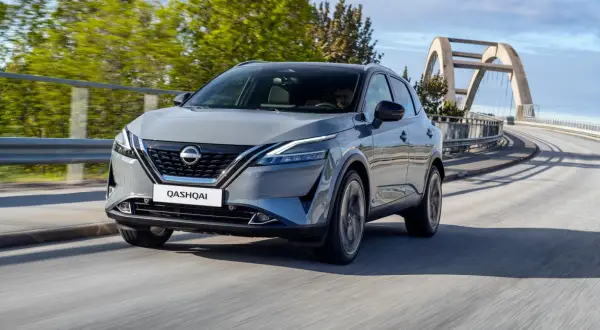 Szary Nissan Qashqai 2024 pędzi po moście z łukowatym wiaduktem w tle.