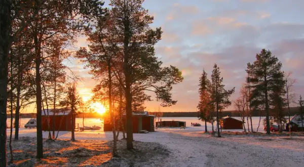 Solnedgång över camp alta kiruna. Röda stugor och snö täcker marken.
