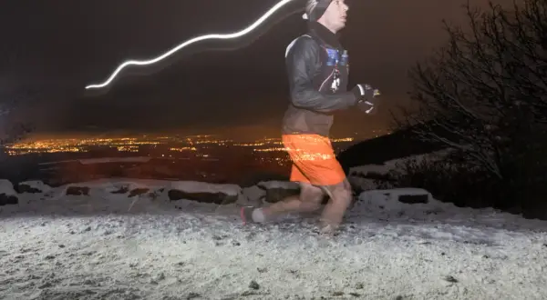 Un coureur nocturne s'entraîne pour la Saintélyon sur un sentier enneigé, la ville illuminée en arrière-plan.