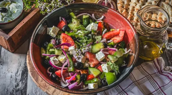 Frischer griechischer Salat mit Feta, Tomaten, Gurken, Oliven und Zwiebeln in einer Schüssel.