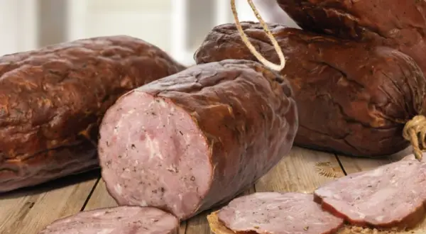 Kiełbasa żywiecka, wędzona, z widocznym przekrojem i plastrami na chlebie, prezentuje się apetycznie na drewnianym stole.