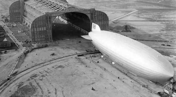 Ogromny hangar lotniczy i sterowiec Hindenburg na płycie lotniska.
