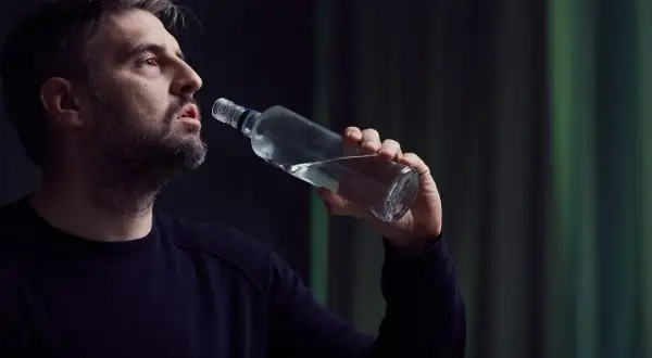 Mężczyzna z siwiejącą brodą pije alkohol z butelki, pogrążony w depresji alkoholowej.