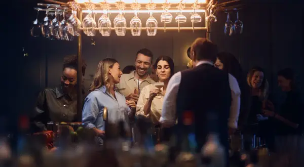 Glada gäster minglar och skrattar vid baren på Gothia Towers Skybar. Glas hänger i taket, redo för drinkar.