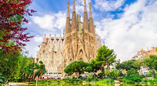 Sagrada Familia, z jej unikalną architekturą i otaczającą zielenią, to miejsce pełne ciekawostek. Woda w stawie odbija majestatyczne wieże.