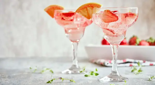 Orzeźwiające drinki z truskawkami i plasterkami grejpfruta, idealne na letnie popołudnie. W tle widać świeże truskawki.