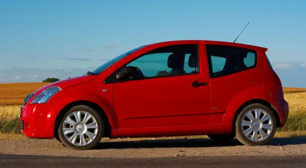 Czerwony Citroen C2 VTR stoi na poboczu drogi, na tle złotego pola i błękitnego nieba.