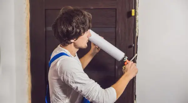 Un homme utilise une mousse expansive pour comment isoler une porte. Il applique le produit dans l'encadrement.