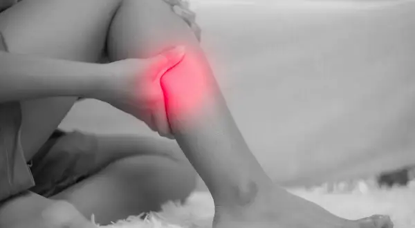 Una persona si tiene la gamba, evidenziata in rosso, per un dolore acuto. Le fitte gambe sono un segnale da non ignorare.