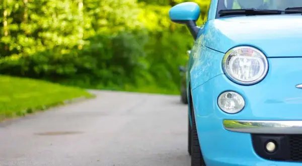 Niemiecki cepik, błękitny Fiat 500, parkuje na krętej drodze wśród zieleni.
