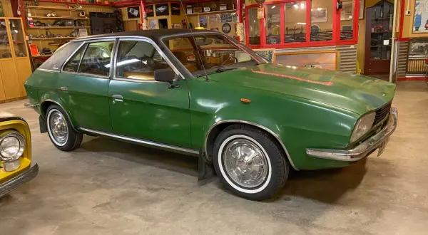 Grön Leyland Princess med svart tak, vit däcksida och kromdetaljer, parkerad i ett garage med retroinredning.