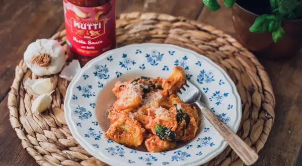 En tallrik med krämig tortellini, toppad med parmesan och färska örter. Bredvid står en burk Mutti tomatsås och vitlök, perfekt för ett enkelt tortellini recept.