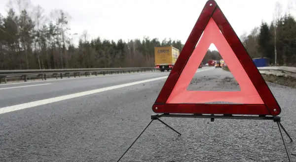 Czerwony trójkąt ostrzegawczy na poboczu drogi, sygnalizujący awarię. W tle ciężarówka i inne pojazdy.